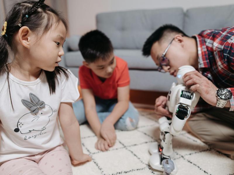 Two children and an adult playing with a white robot